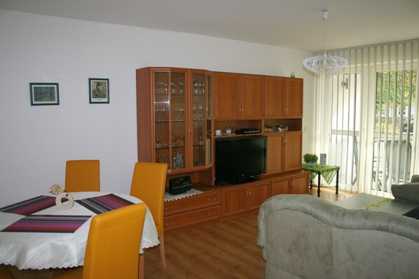 Un soggiorno con zona pranzo, mobili contenitori in legno, una televisione e un divano.