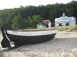 Un bote en una playa arenosa con un bosque y edificios al fondo.