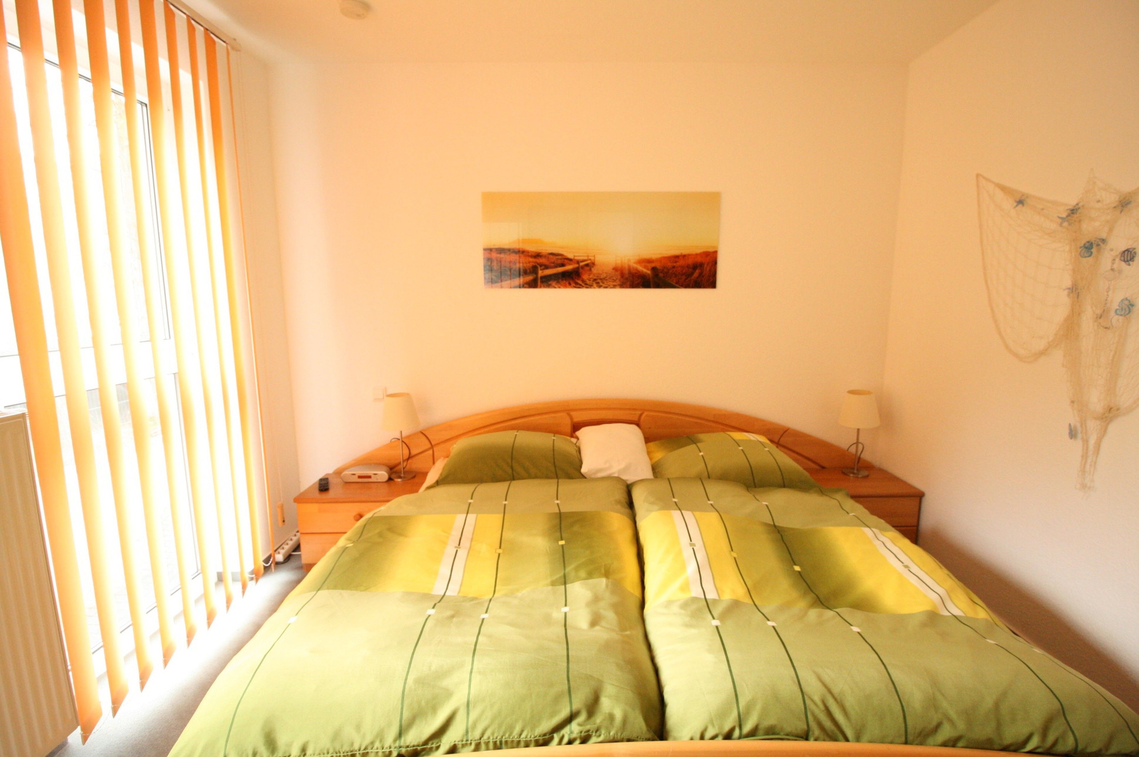 A bedroom with a bed, bedside tables, a painting on the wall, and a window with blinds.