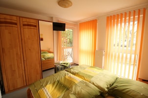 A bedroom with a bed, a wardrobe, a television, and a window with curtains.