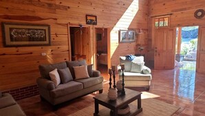 A wooden cabin interior with a sofa, a chair, and a coffee table. There are framed pictures on the walls and a door leading outside. - Green Resort (San Martín Jilotepeque)