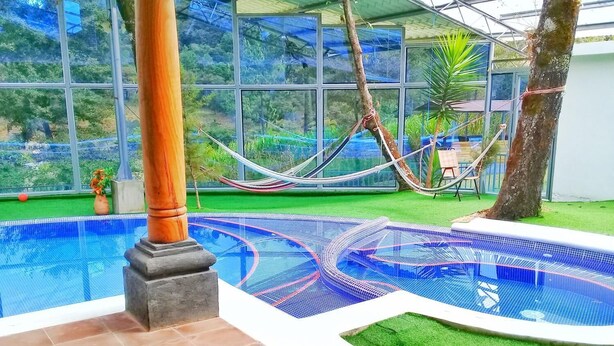 An indoor swimming pool with a unique design, surrounded by artificial grass and a glass enclosure with a view of greenery outside. - Green Resort (San Martín Jilotepeque)