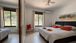 A hotel room with two beds, a ceiling fan, an air conditioning unit, and a painting on the wall.