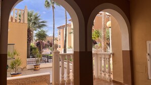 A corridor with arches leading to a courtyard with palm trees and a pool.