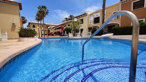 A swimming pool with a tiled edge, surrounded by palm trees and a building with balconies.