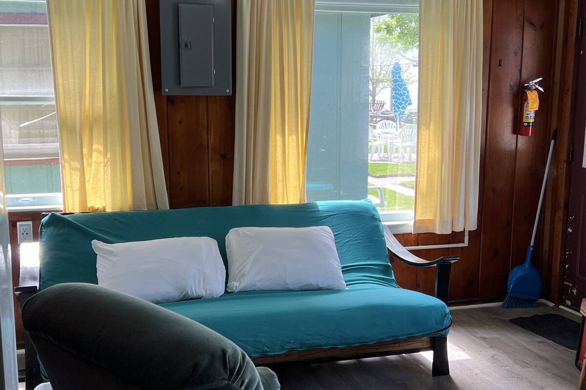 A teal sofa with white cushions, a wooden floor, a broom, and a fire extinguisher.