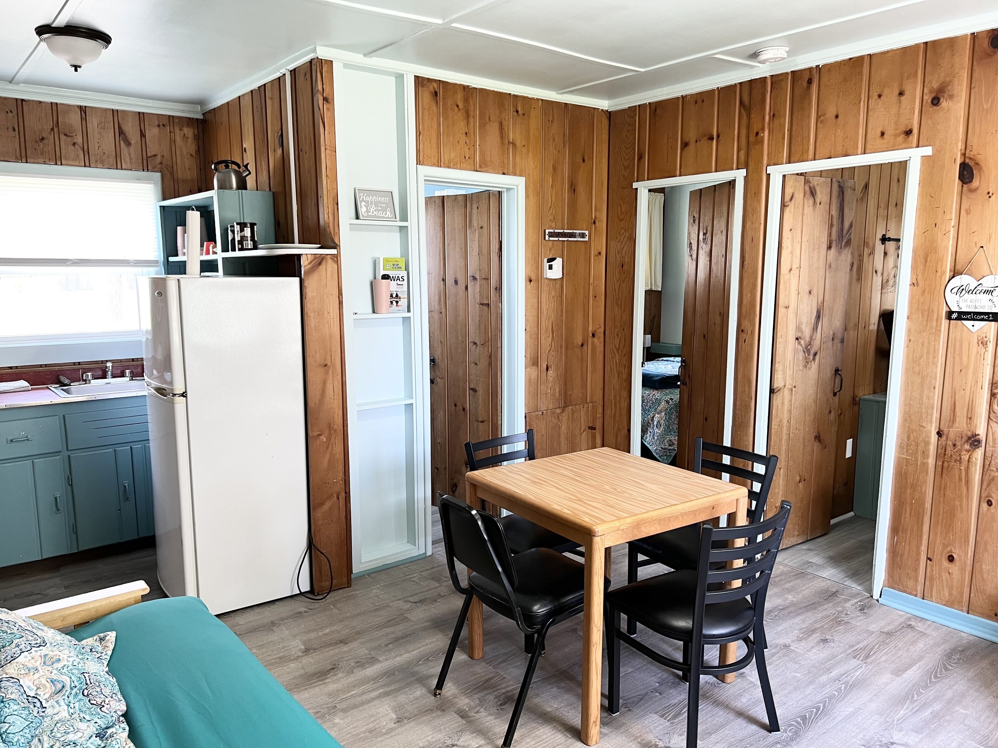 Une pièce de taille modeste avec un mur en bois, un coin cuisine, une table à manger avec des chaises et un lit.