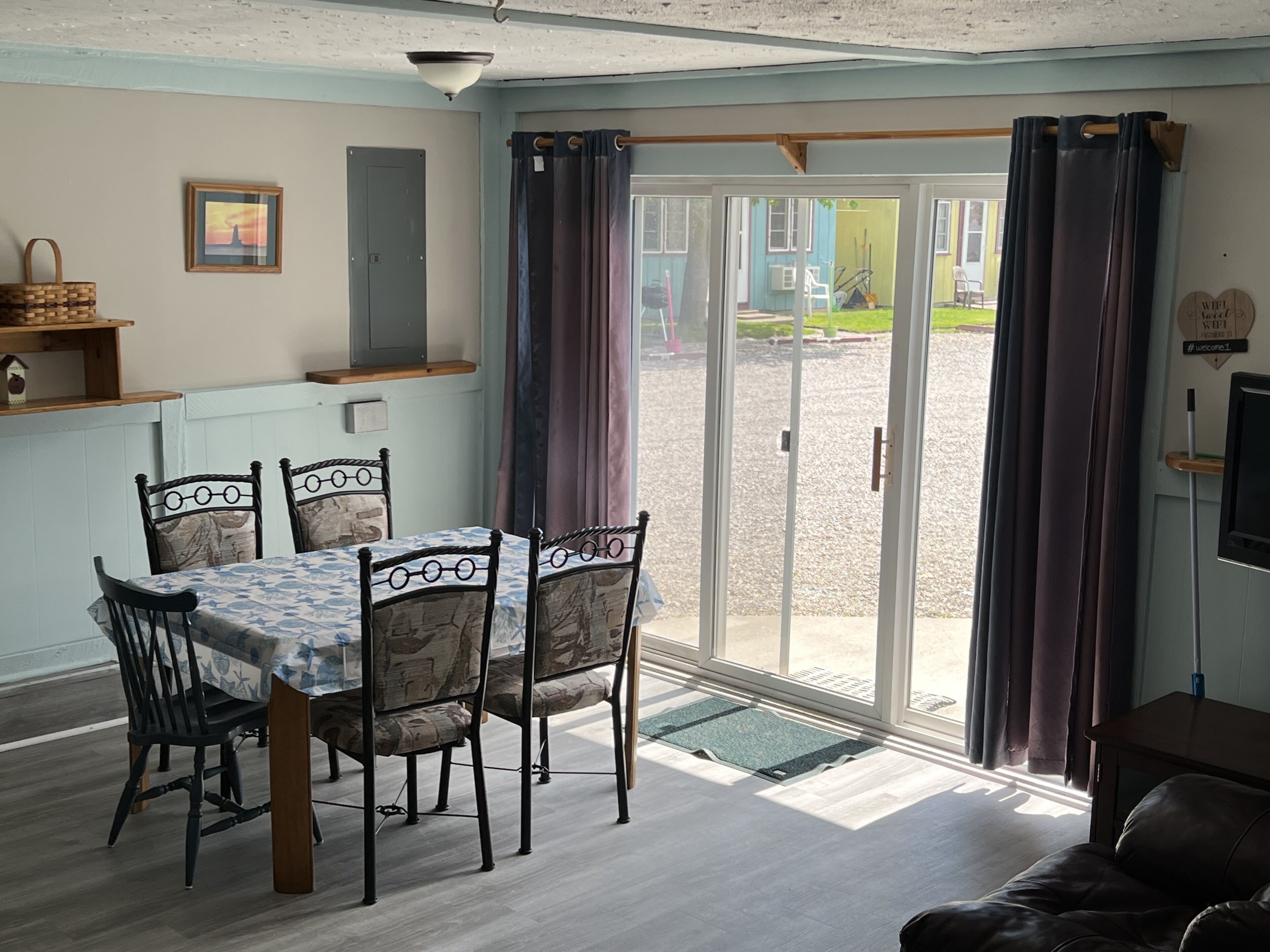 Un comedor con mesa y sillas, una cocina con pileta y muebles bajos, y un ventanal corredero que da a un patio exterior.
