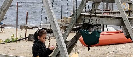 A wooden swing set on a sandy beach with a body of water in the background.