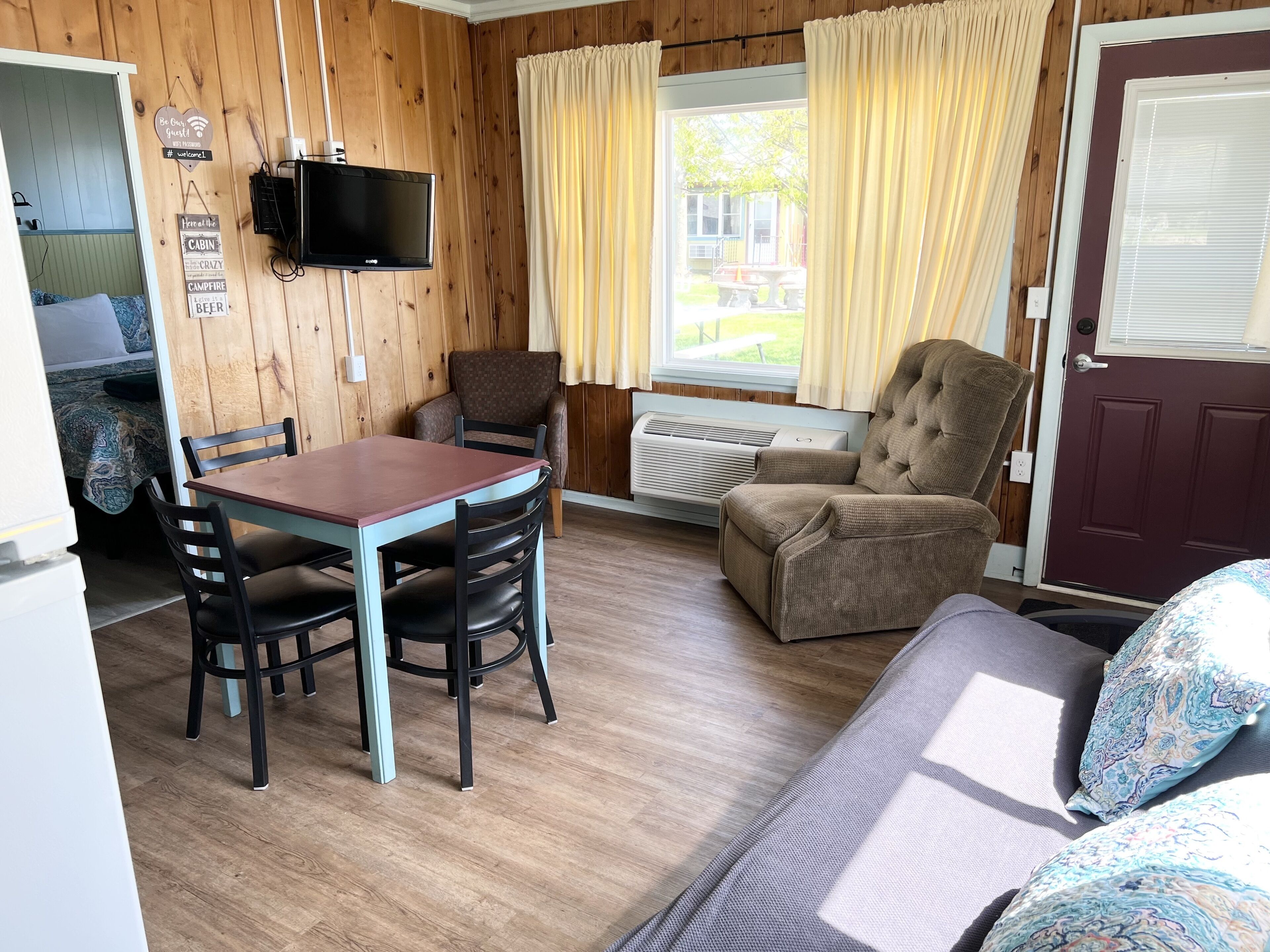 Una habitación acogedora de estilo cabaña con interior de madera, una mesa de comedor con sillas, un sillón cómodo y un televisor montado en la pared.