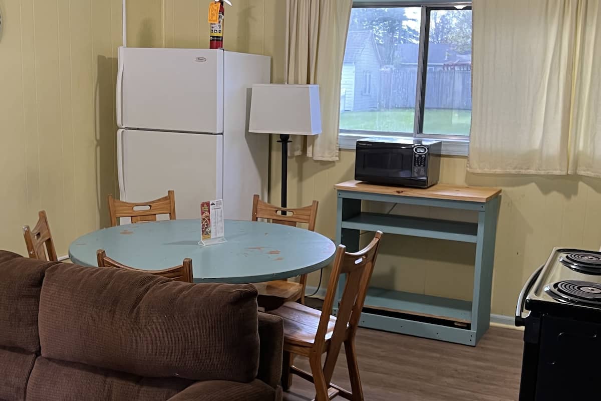 A compact kitchen with a refrigerator, microwave, and stove. There is a dining table with chairs and a couch in the foreground.