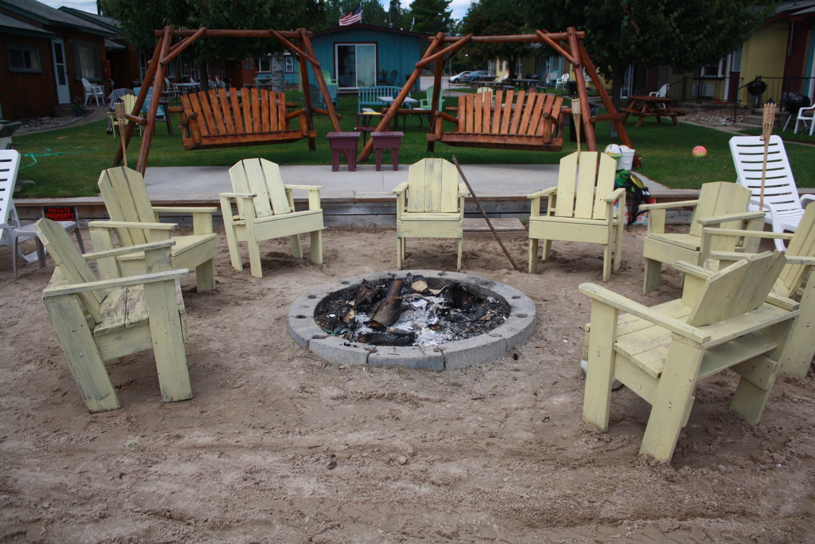 A sandy outdoor area with a circular fire pit surrounded by wooden chairs.