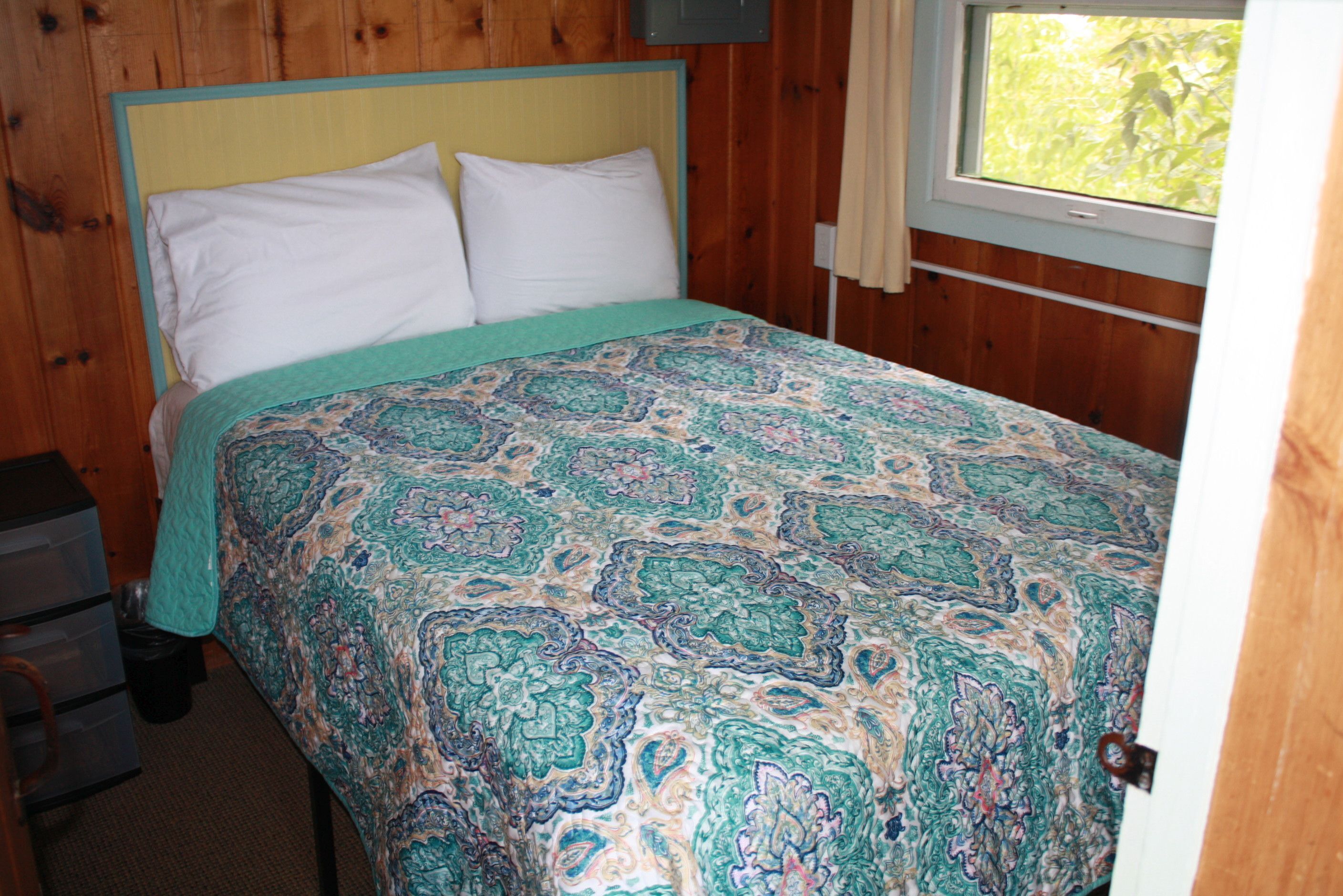 A bedroom with a bed, wooden walls, a window, and a door.
