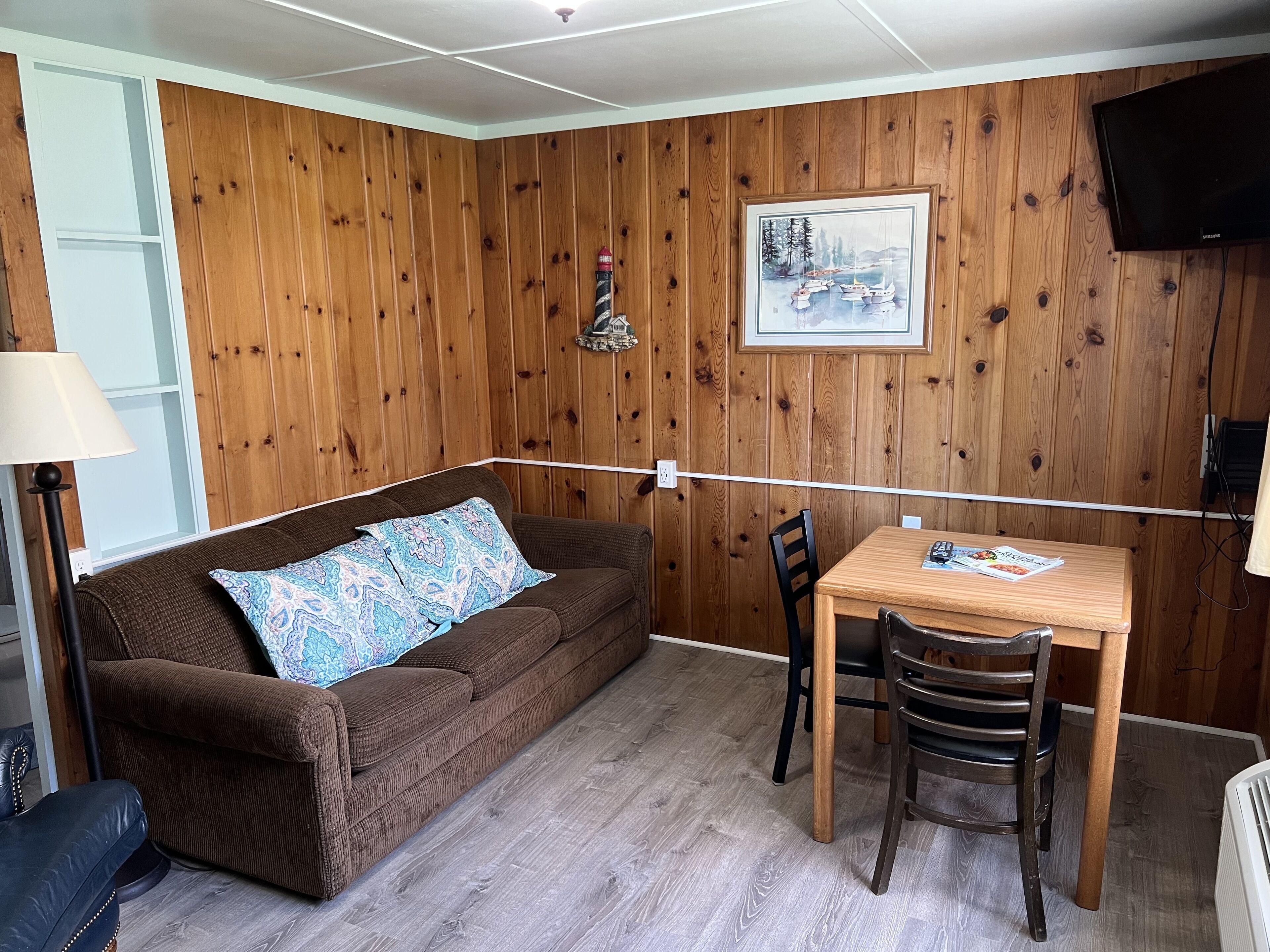 Una habitación acogedora con un sofá marrón, una mesa de comedor de madera y un televisor montado en la pared.