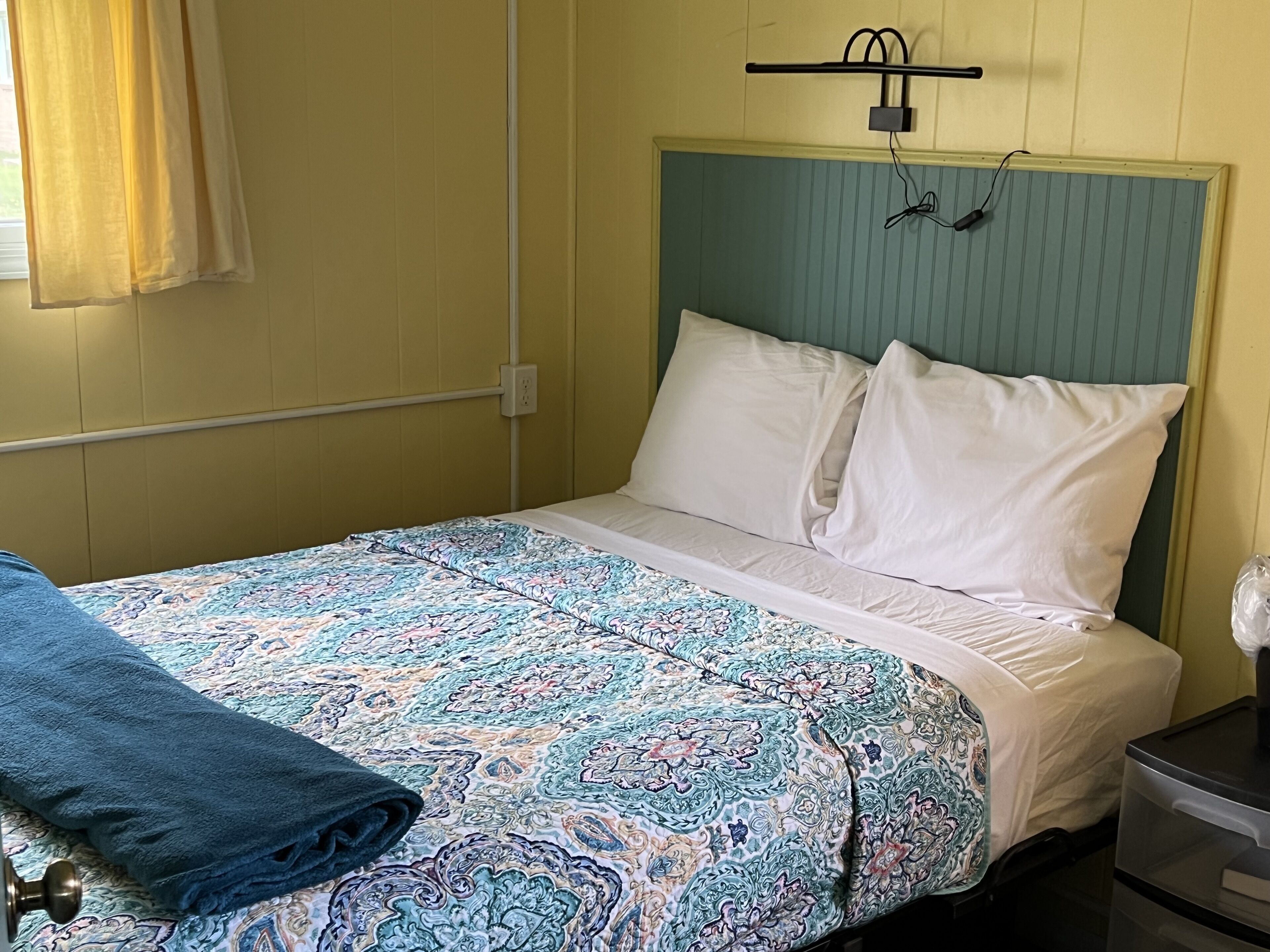 Una cama individual con una colcha estampada, almohadas blancas y una manta azul.