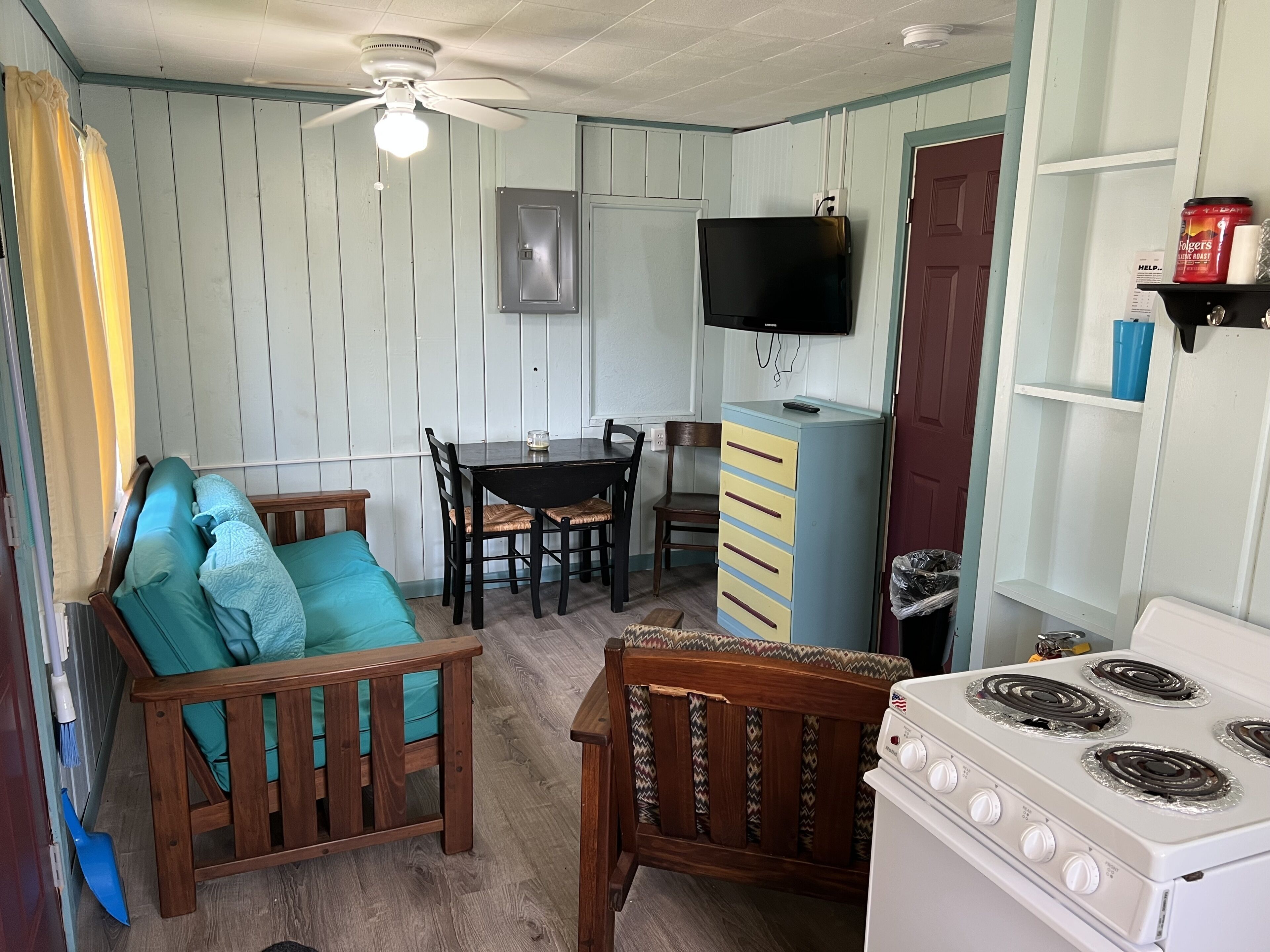 A compact kitchen with a stove, a dining table with chairs, a small refrigerator, and a ceiling fan.