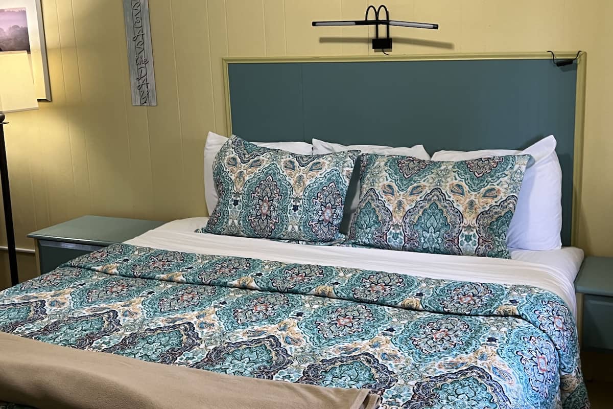 A neatly made bed with patterned bedding, a bedside table, and a wall-mounted lamp.