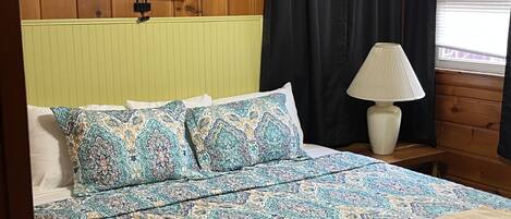 A bed with patterned bedding, a bedside lamp, and wooden paneling on the walls.