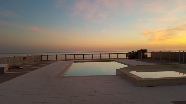 A rooftop pool with a view of the ocean at sunset.