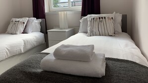 Ein Hotelzimmer mit zwei Einzelbetten, einem Nachttisch, einem Fenster mit Vorhängen und Blick ins Freie.