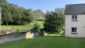 Ein Rasen mit einer Steinmauer, einem Baum und einem Gebäude mit Satteldach.