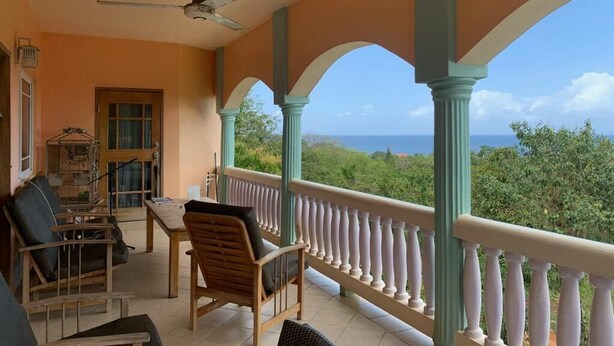 A covered balcony with a view of the sea, featuring a table and chairs, a ceiling fan, and a birdcage. - Jah Freedom Inn Negril (Negril)