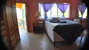 A bedroom with a bed, a nightstand, a lamp, and a window with purple curtains. - Jah Freedom Inn Negril (Negril)