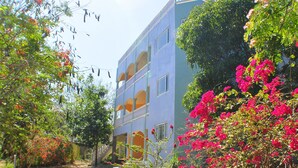 A multi-story building with balconies, surrounded by lush greenery and vibrant pink flowers. - Jah Freedom Inn Negril (Negril)