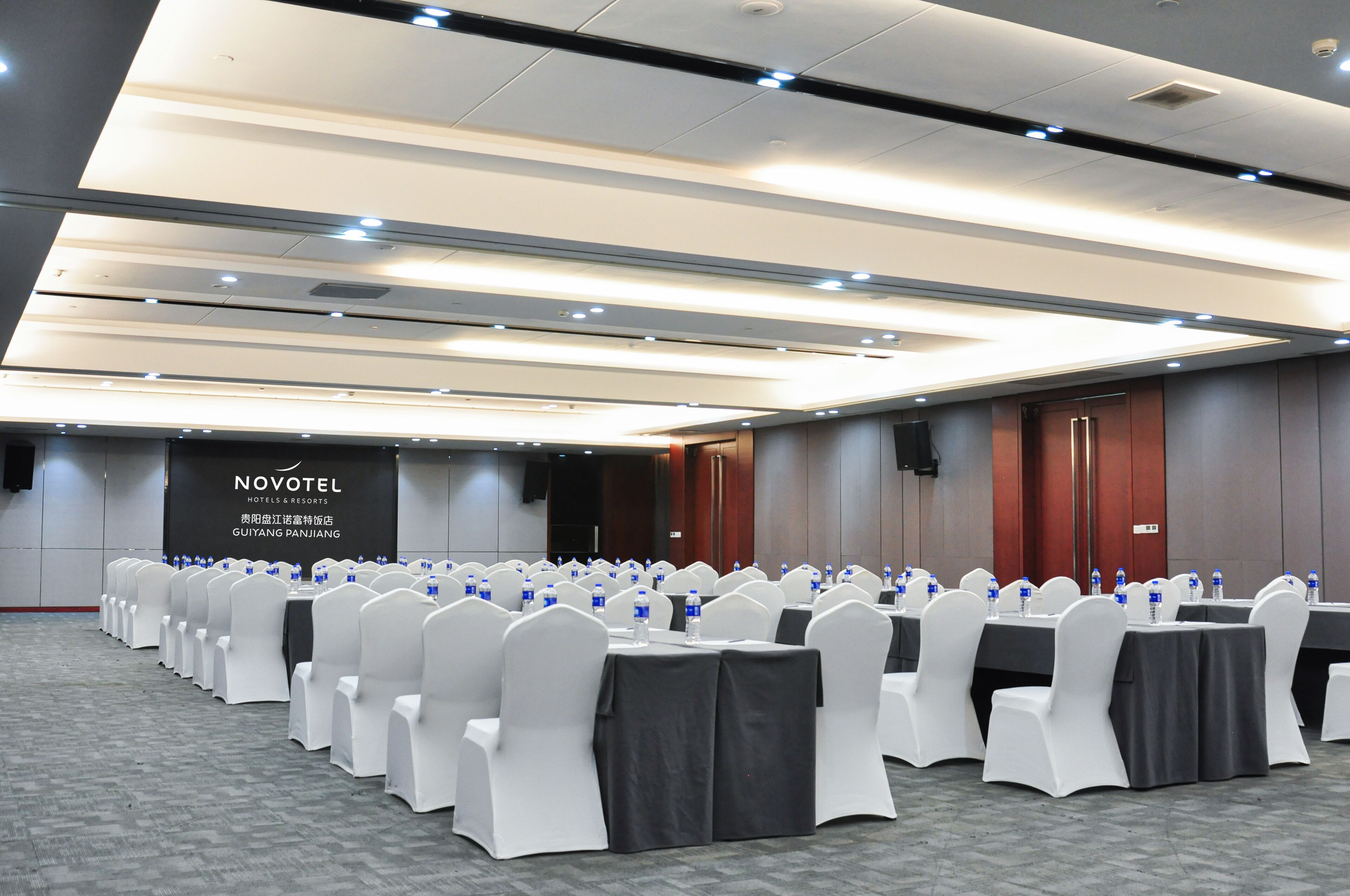 Una sala de conferencias con filas de mesas y sillas, un cartel con el nombre del hotel y suelo alfombrado.