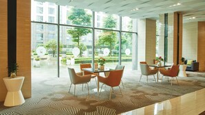Un hall moderno con pared de vidrio, piso estampado y zona de comedor con sillas naranjas y una mesa.