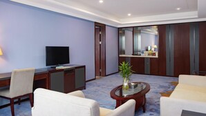 Una habitación de hotel con televisión, escritorio, sillas, una mesa de centro y un espejo.
