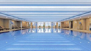 Una amplia piscina cubierta con agua cristalina, rodeada de sillones de descanso y paneles de madera.