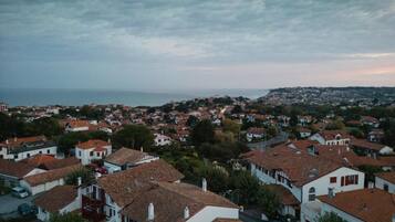 Ein Wohngebiet mit Häusern mit roten Ziegeldächern und weißen Wänden, umgeben von viel Grün und einem Blick auf das Meer in der Ferne.