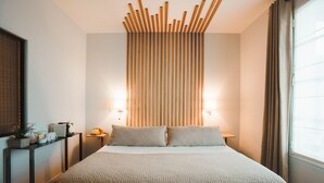 Habitación de hotel moderna con una cama grande, una mesita de noche con lámpara, un panel de luz en la pared y una ventana con cortinas.
