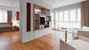 Una sala de estar moderna con televisión empotrada, piso de madera, sofá, una mesita y un banco.