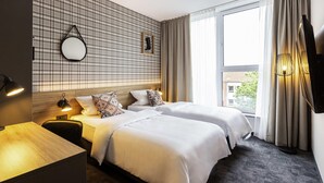 Habitación de hotel con dos camas, un escritorio de madera, un espejo, un televisor montado en la pared y una ventana con cortinas.