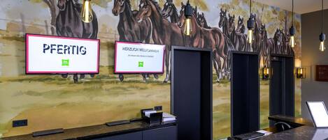 Una recepción con un mural de caballos, dos letreros de bienvenida enmarcados y una lámpara moderna.