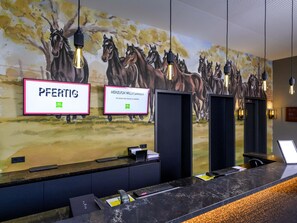 Una recepción con un mural de caballos, dos letreros de bienvenida enmarcados y una lámpara moderna.