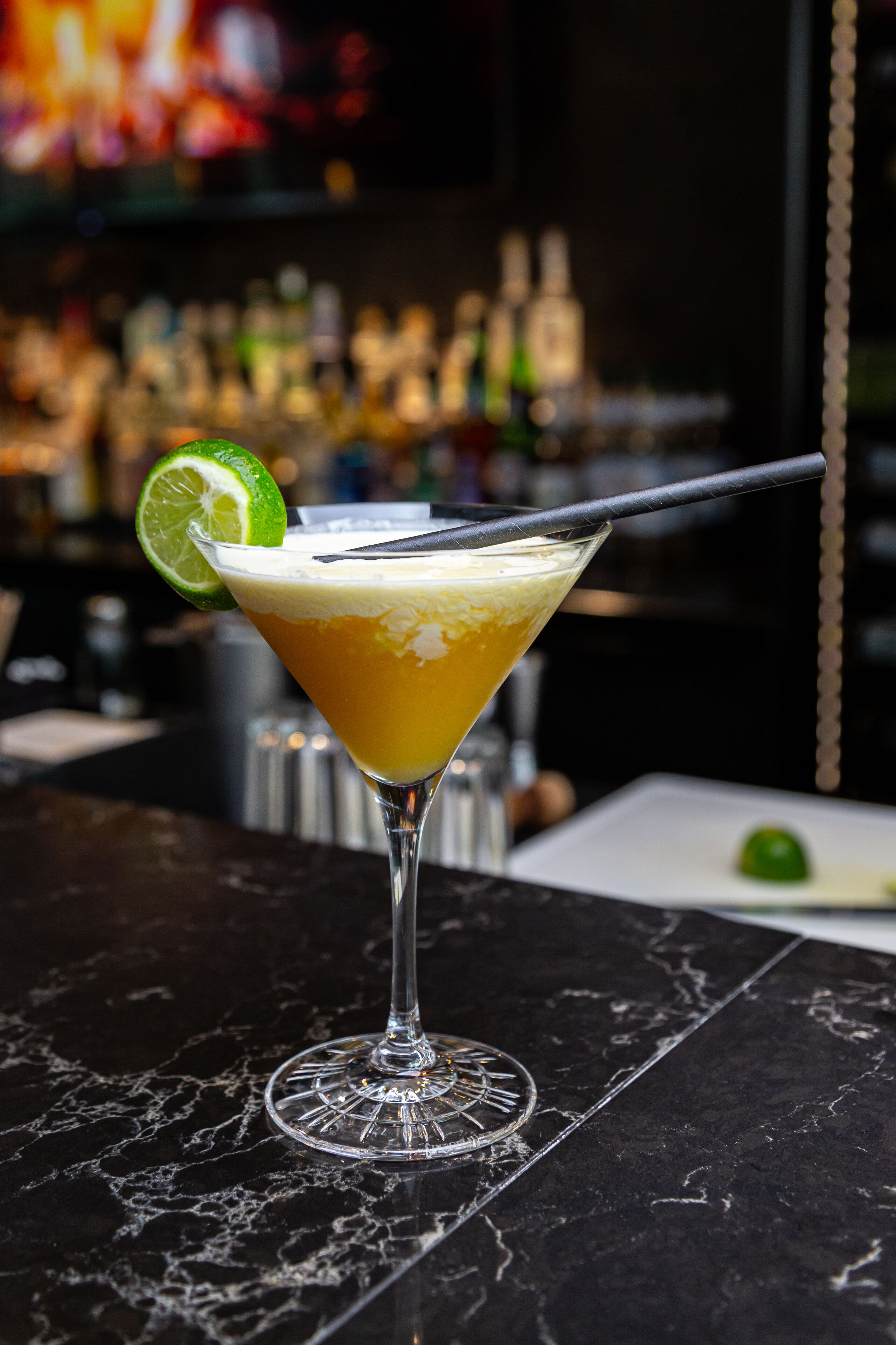 A martini glass with a lime garnish on a marble surface.