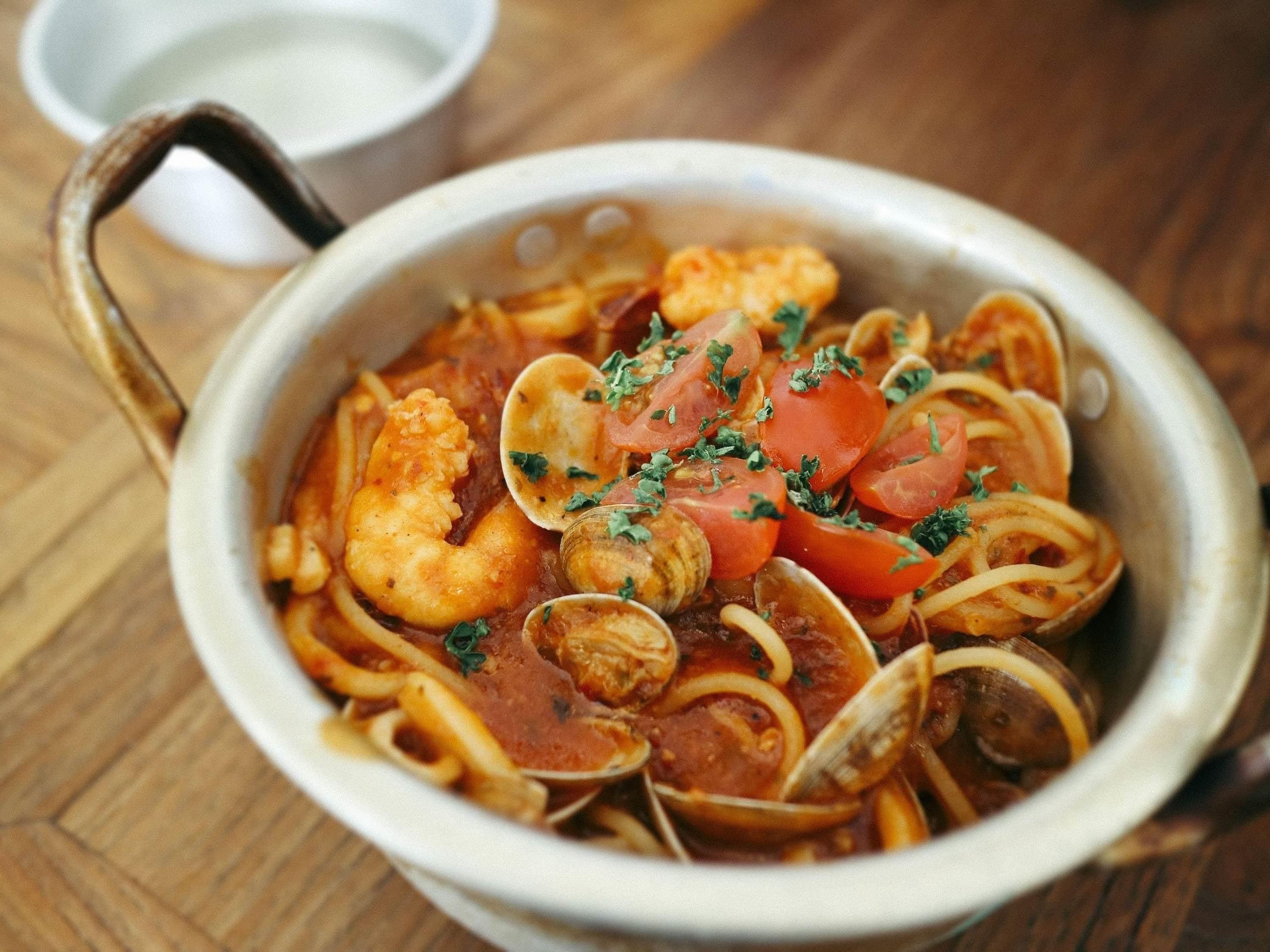 A bowl of seafood pasta with clams, shrimp, and tomatoes, garnished with herbs.