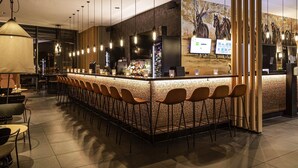 Una zona de bar con una barra alargada, varios taburetes y lámparas colgantes.