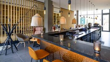 A modern bar area with a marble countertop, bar stools, pendant lighting, and a view of the city through large windows.