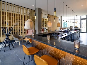 Zona de bar moderna con encimera de mármol, taburetes, iluminación colgante y vistas a la ciudad a través de amplios ventanales.