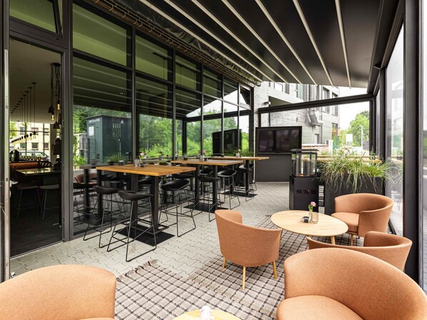 Un área de comedor al aire libre con mesas, sillas, un televisor y una parrilla.