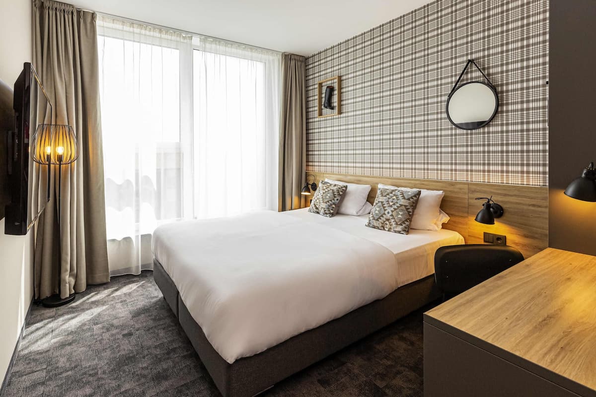Hotellihuone, jossa on suuri sänky, työpöytä, peili ja näkymä kaupunkiin.