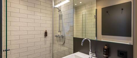 Un baño moderno con ducha acristalada, lavamanos blanco y un espejo grande.
