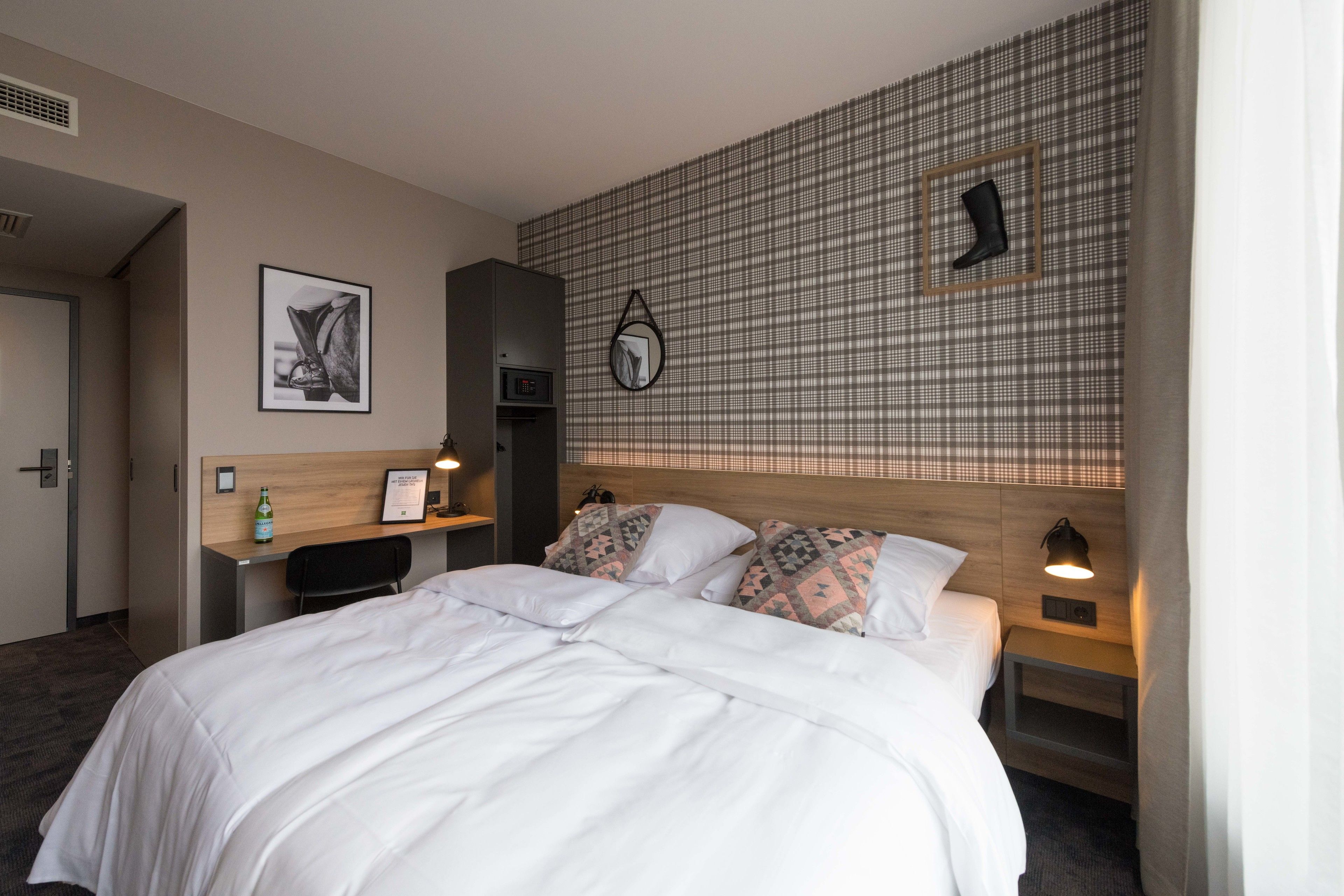 Une chambre d’hôtel avec un grand lit, un bureau, une chaise, une petite table, une horloge murale et une lampe fixée au mur.
