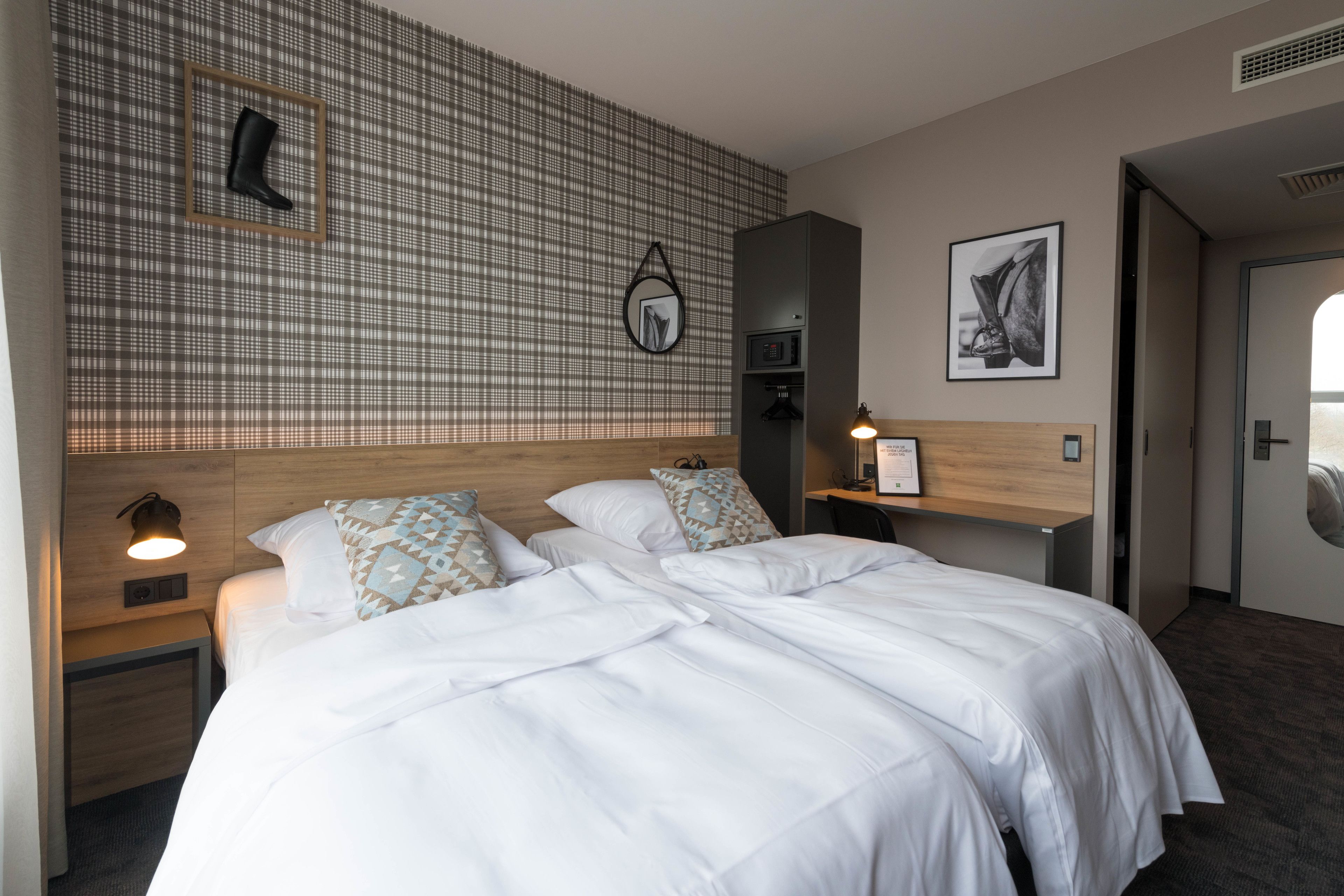Habitación de hotel con dos camas, un muro a cuadros, un cuadro colgado y un pequeño estante con un marco de fotos.