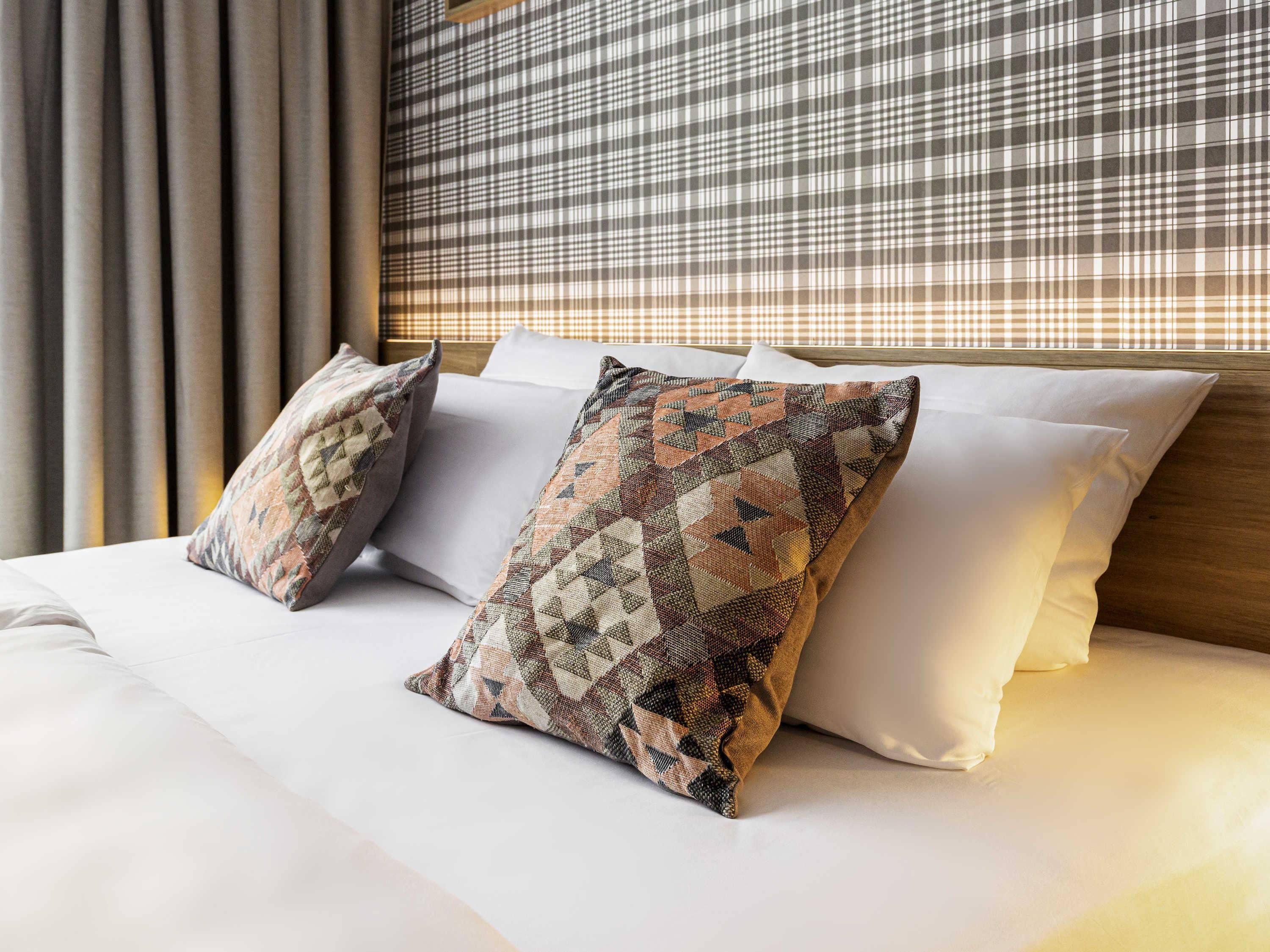 A hotel room with a bed, pillows, and a checkered headboard.