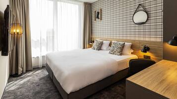 Habitación de hotel con una cama grande, un escritorio, un espejo y vistas a la ciudad.